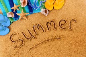 The word Summer written on a sandy beach, with scuba mask, beach towel, starfish and flip flops (studio shot - warm color and directional light are intentional).